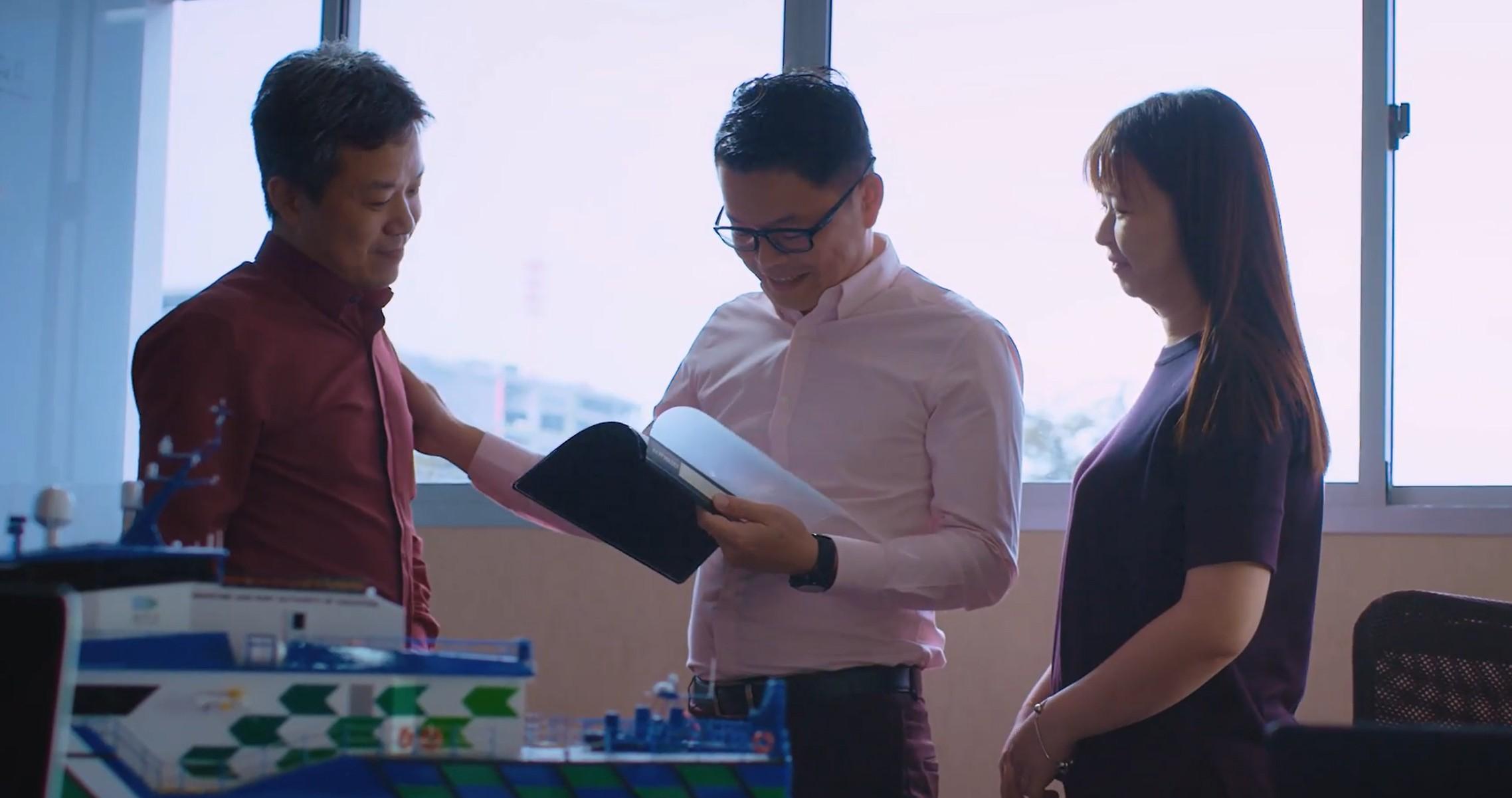 two men and 1 woman in business attire, looking at 1 document held by the man in the middle